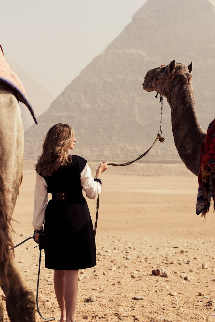 Woman with camel in desert by Giza Pyramids, capturing Egypt's iconic landscape and culture.
